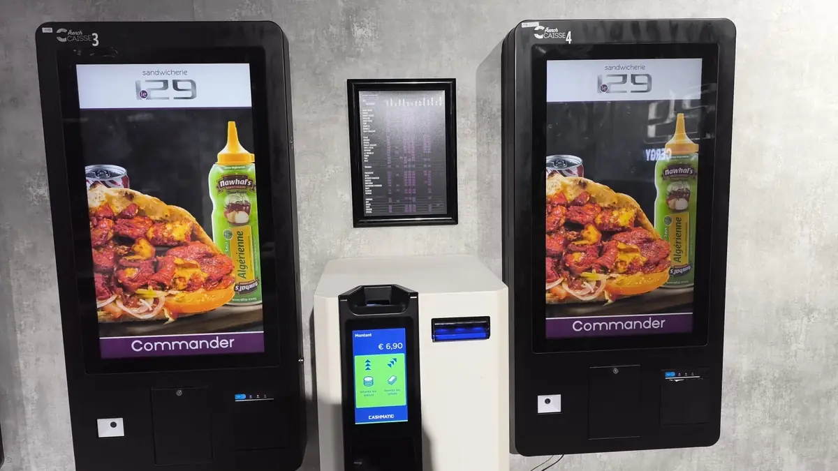 Deux bornes de commande VisualPay fixées au mur, encadrant un monnayeur automatique